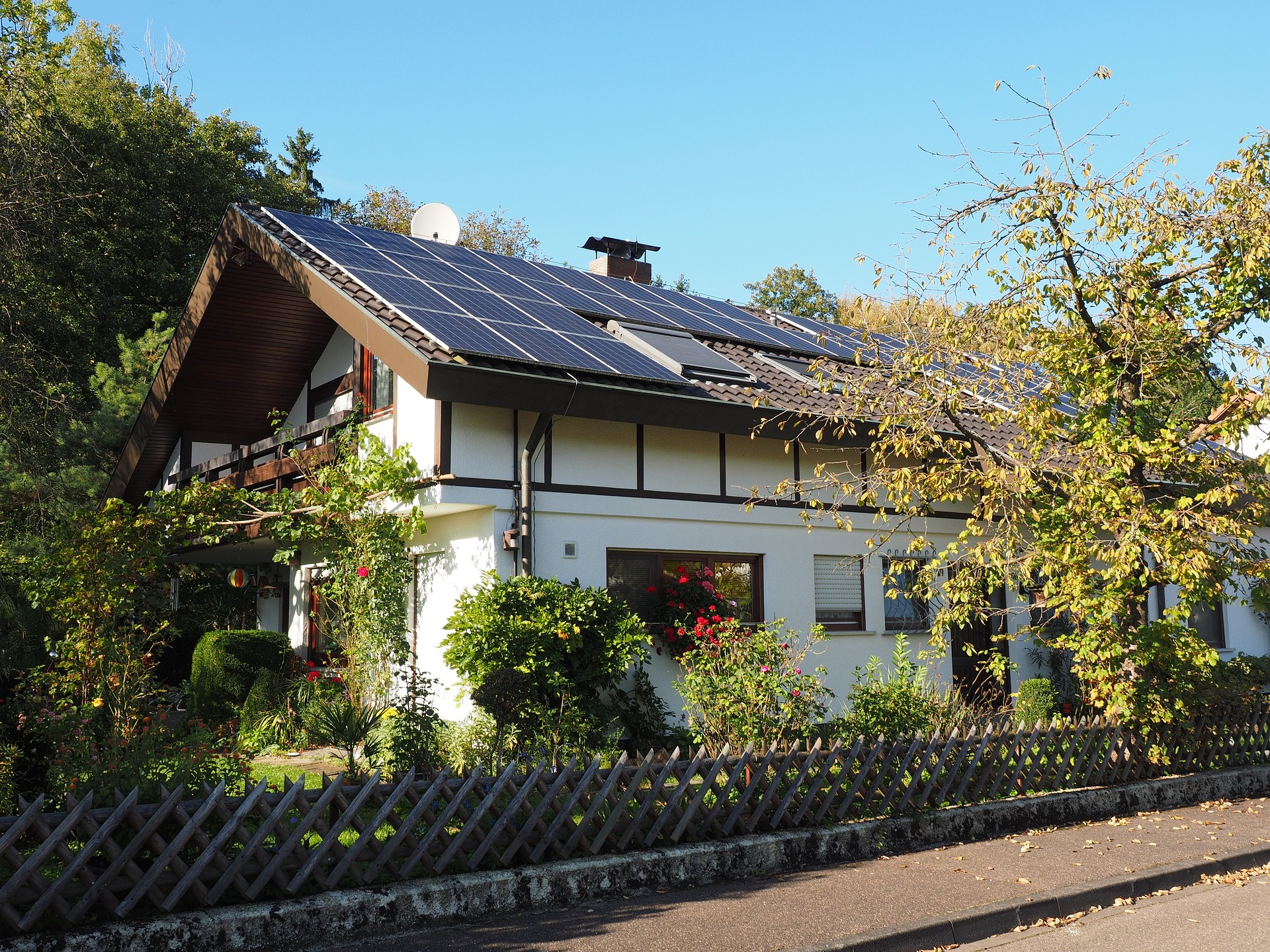 Ein weißes Haus mit einem begrünten Garten und einer PV-Anlage auf dem Dach.