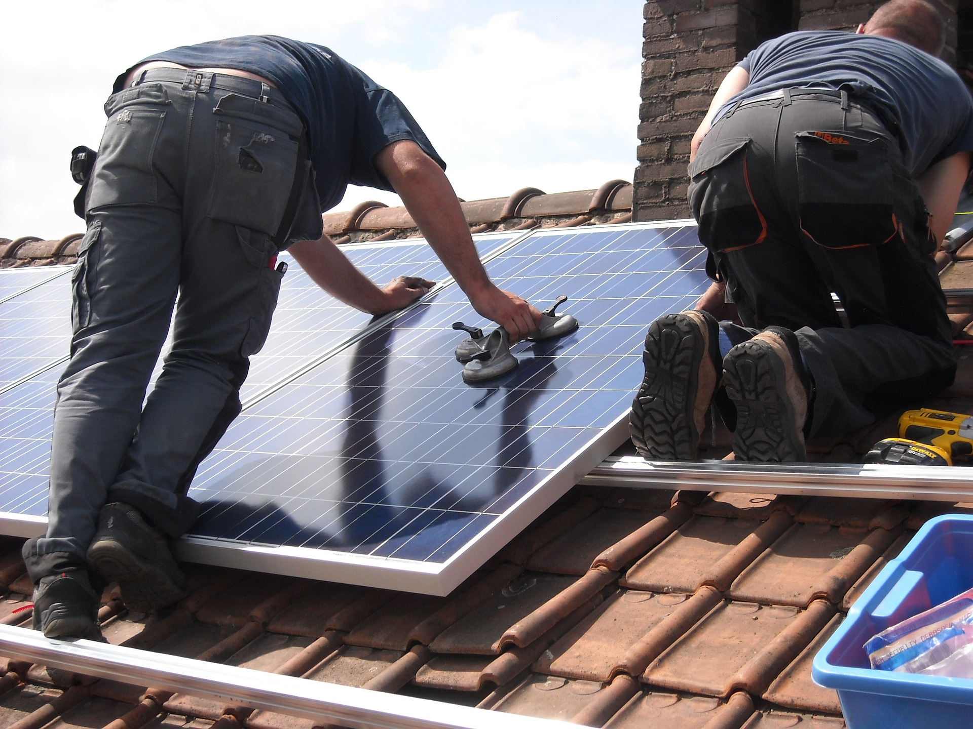 Zwei Handwerker auf Schrägdach montieren zwei Monokristalline Solarmodule mit Dachpfannen-System.